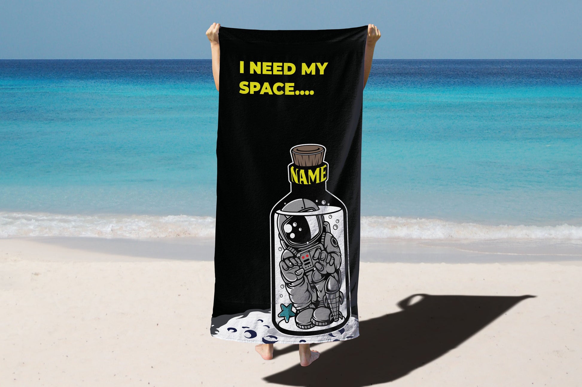 A person holding a 'I need my space' beach towel on a beach background