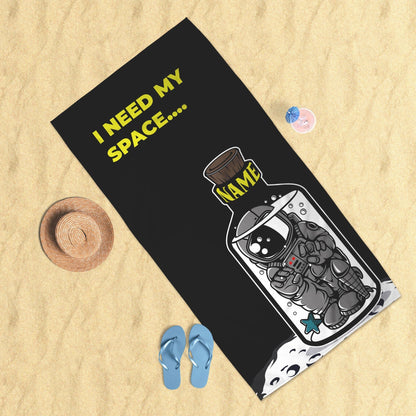 An 'I need my space' beach towel lying on beach surface, hat, slipper & drink on the side