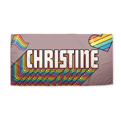 A retro rainbow heart beach towel with 'Christine' printed on white surfce