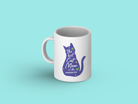 White ceramic mug with "You are the BEST Cat Mom in the Universe!" printed in bold letters against a galaxy background, featuring playful cat illustrations.