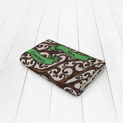 Folded beige blanket with an intricate brown and green design featuring the names "Alex" and "Courtney" on green banners.