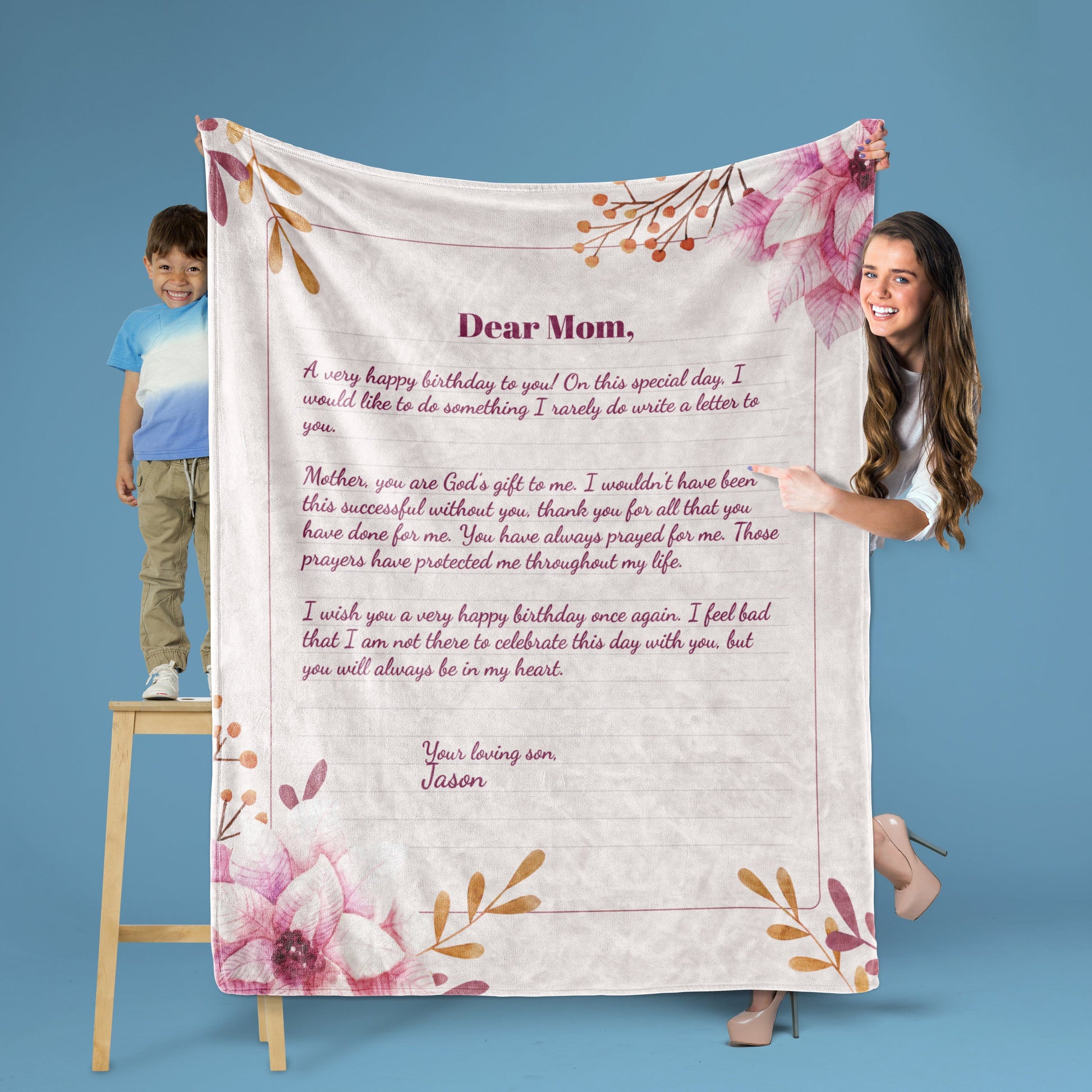 A lady and a kid on stool holding a custom letter pink floral throw blanket on a blue background