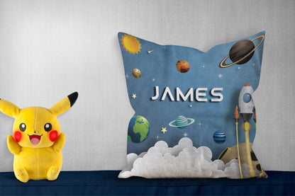 Personalized pillow with "James," showing a rocket, planets, and stars against a blue sky with clouds, pikachoo soft toy on side