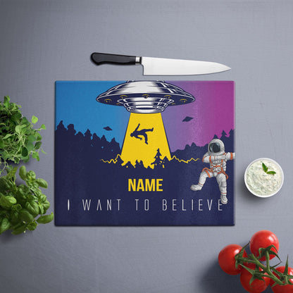 A glass cutting board with a lost in space design on a grey surface and knife & veggies on the side