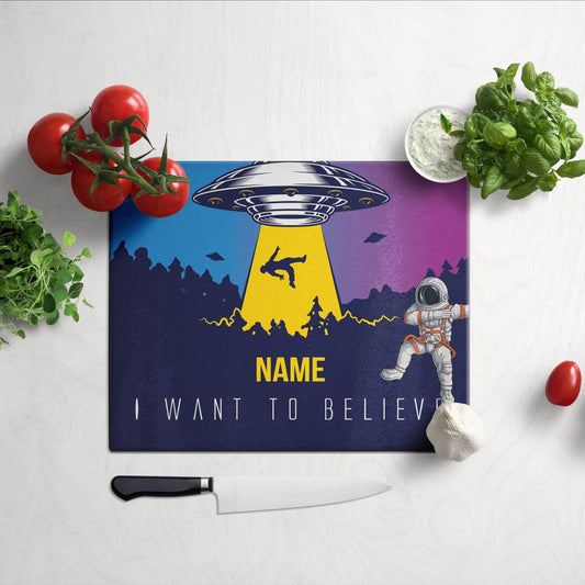 A glass cutting board with an alien invasion design cherry tomatoe, veggies and knife on side