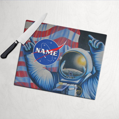 A glass cutting board with an illustration of an astronaut floating in space, surrounded by US flag,stars and planets, with customized name