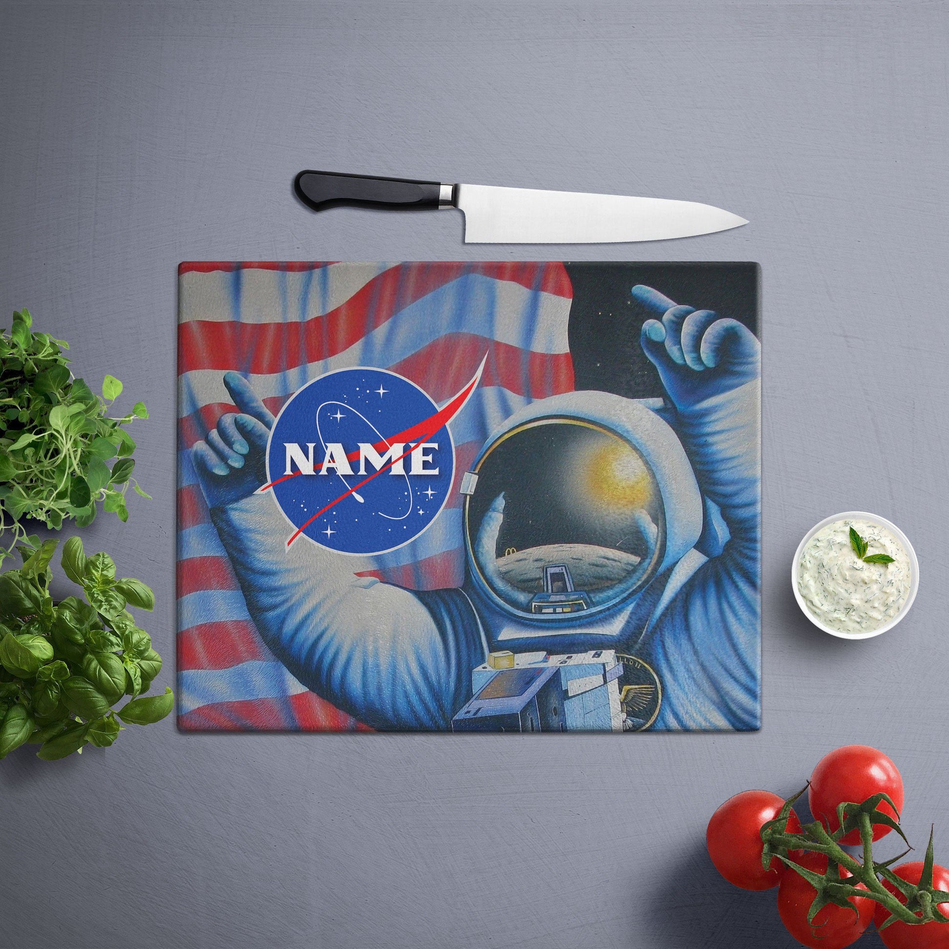 Astronaut in space suit, pointing at American flag, NASA logo visible, text overlay with name, vegetables and knife on the side