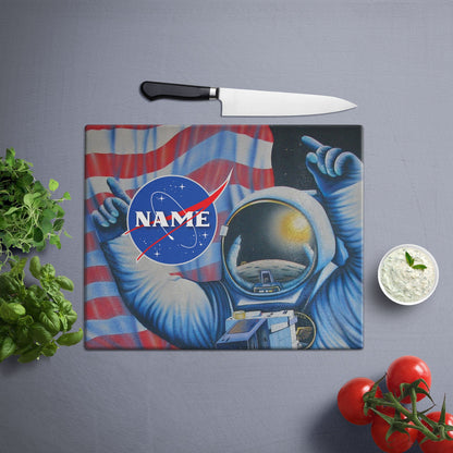 Astronaut in space suit, pointing at American flag, NASA logo visible, text overlay with name, vegetables and knife on the side