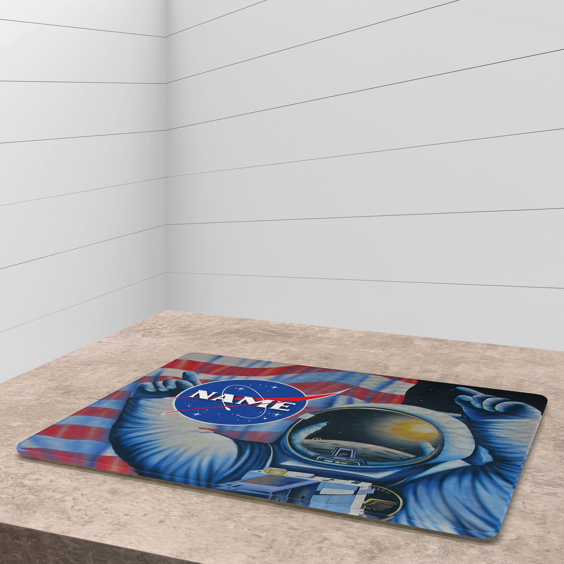 A glass cutting board with an illustration of an astronaut floating in space, surrounded by US flag,stars and planets, on a light brown surface