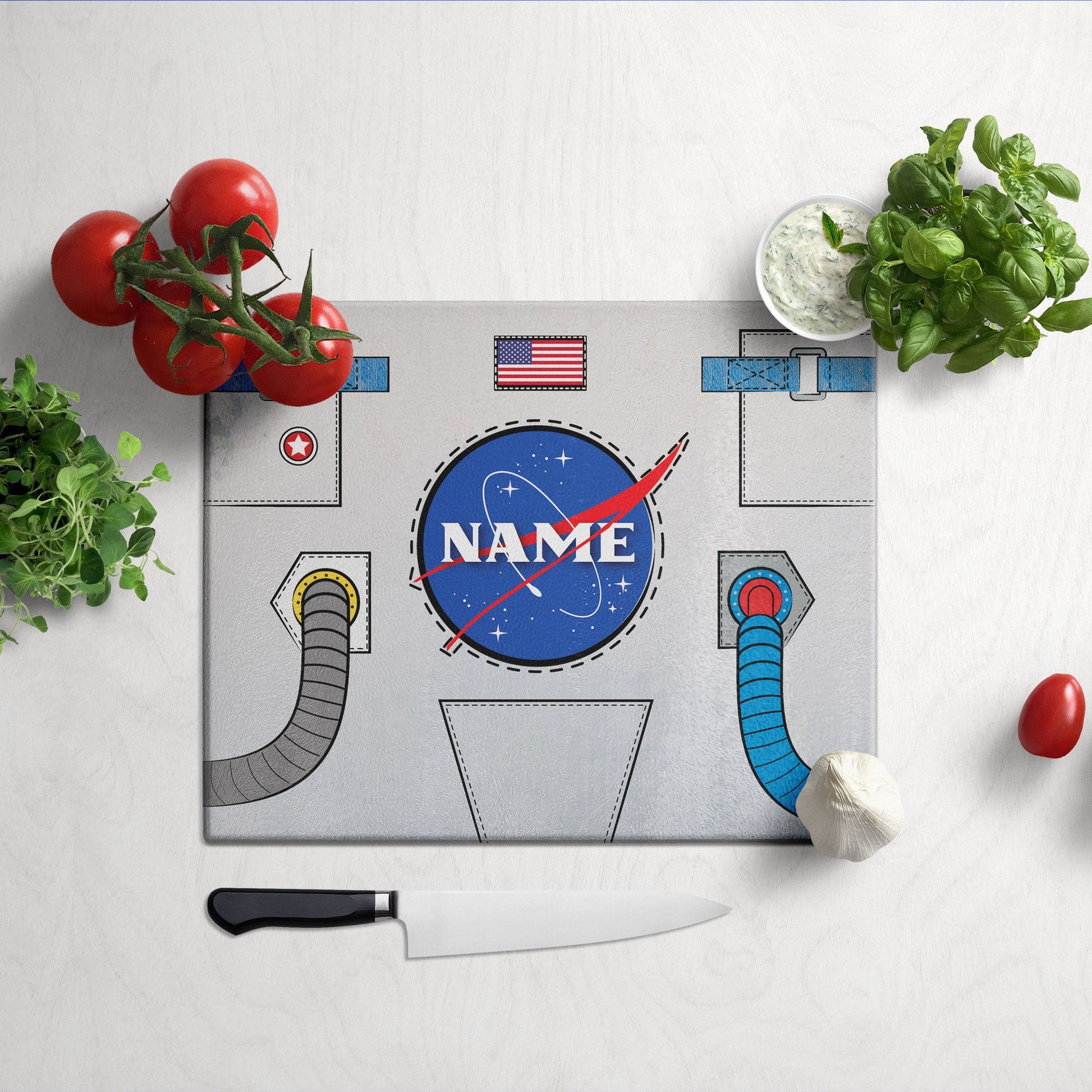 A glass cutting board with astronaut design on a grey surface and knife & veggies on the side