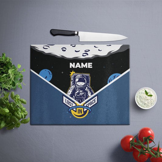 A glass cutting board with an illustration of an astronaut floating in space, surrounded by stars and planets, with customized name and lost in space written