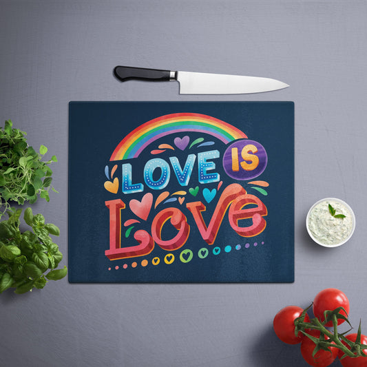 Glass cutting board with 'love is love' printed , placed on a gray surface with a knife, herbs, and cherry tomatoes nearby.