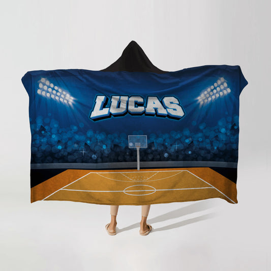 Person wearing a hooded fleece blanket with a basketball stadium design, featuring the name "Lucas" in bold letters