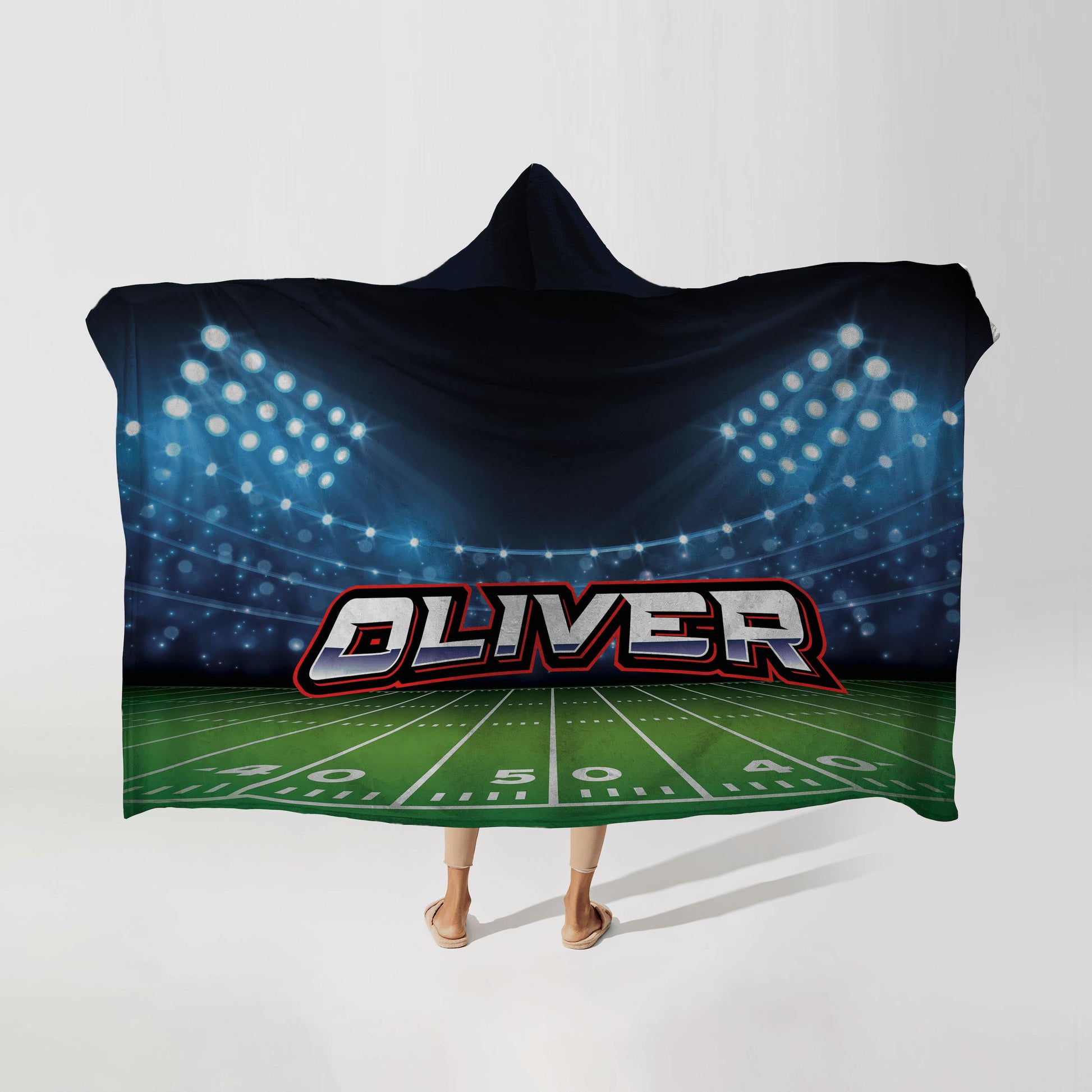 Person wearing a hooded fleece blanket with a Footbal stadium design, featuring the name "Oliver" in bold letters