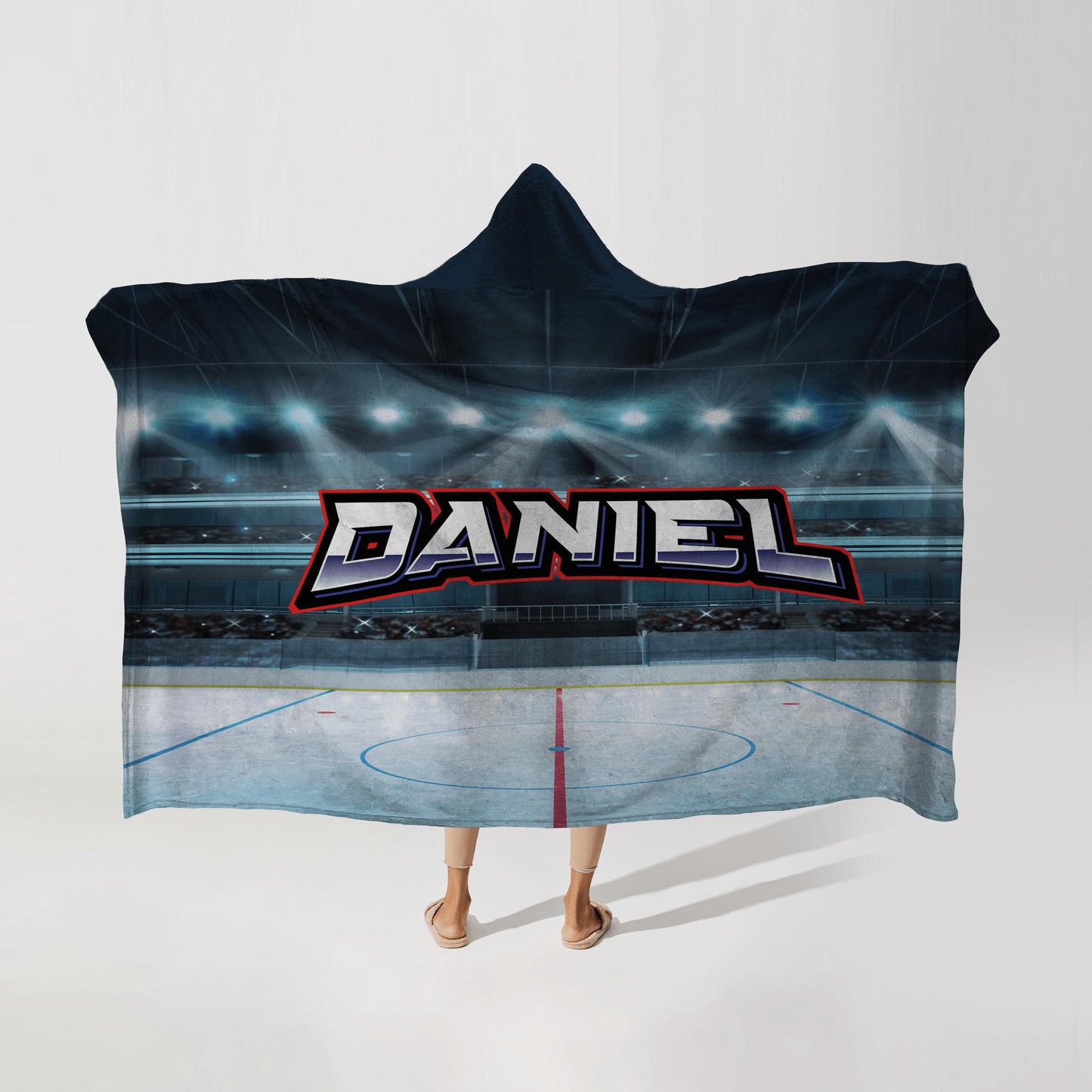 Person wearing a hooded fleece blanket with a hockey rink design, featuring the name "Daniel" in bold letters