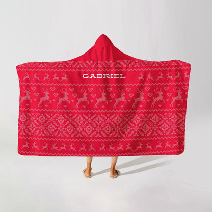 A person wearing a red hooded blanket with christmas patterns in grey and the name "Gabriel" at the top-center on a white background.