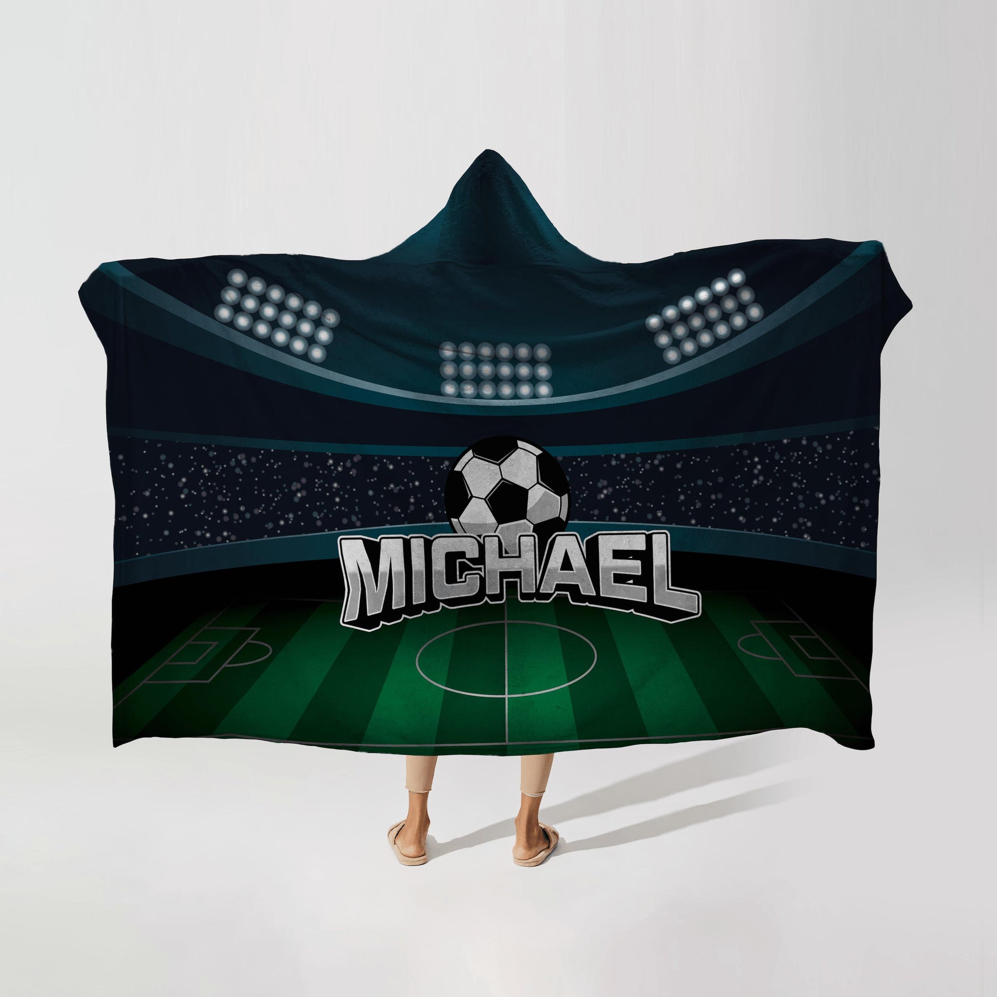 Person wearing a hooded fleece blanket with a soccer stadium design, featuring the name "Michael" in bold letters