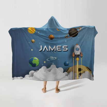 Person wearing a hooded fleece blanket with a spaceship and planet design, featuring the name "James" in bold letters