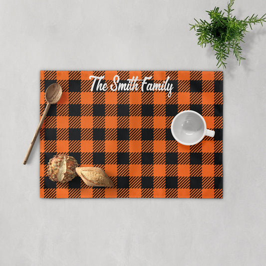 Personalized orange black pattern placemat with "The Smith Family" text and fall leaves, surrounded by bread, spoon, cup, and a plant.