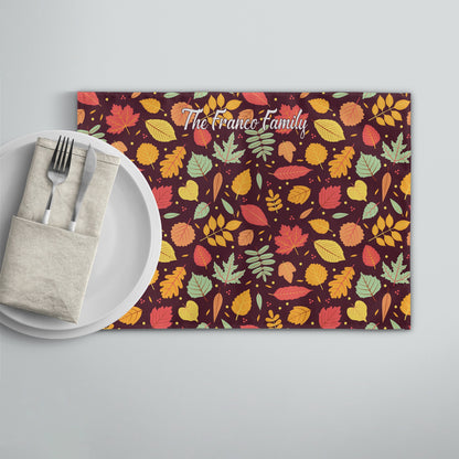 Personalized placemat with "The Franco Family" text, fall leaves pattern, and a white plate, napkin, fork, and knife on the side.