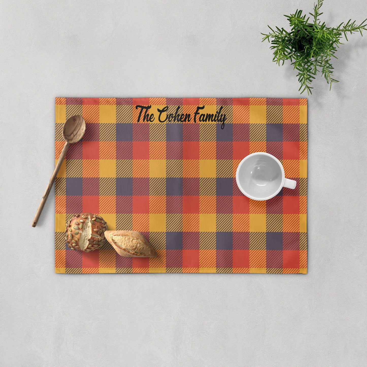 Personalized fall plaid placemat with lavender and pumpkin colors on a wooden table, featuring a name with autumn leaves.