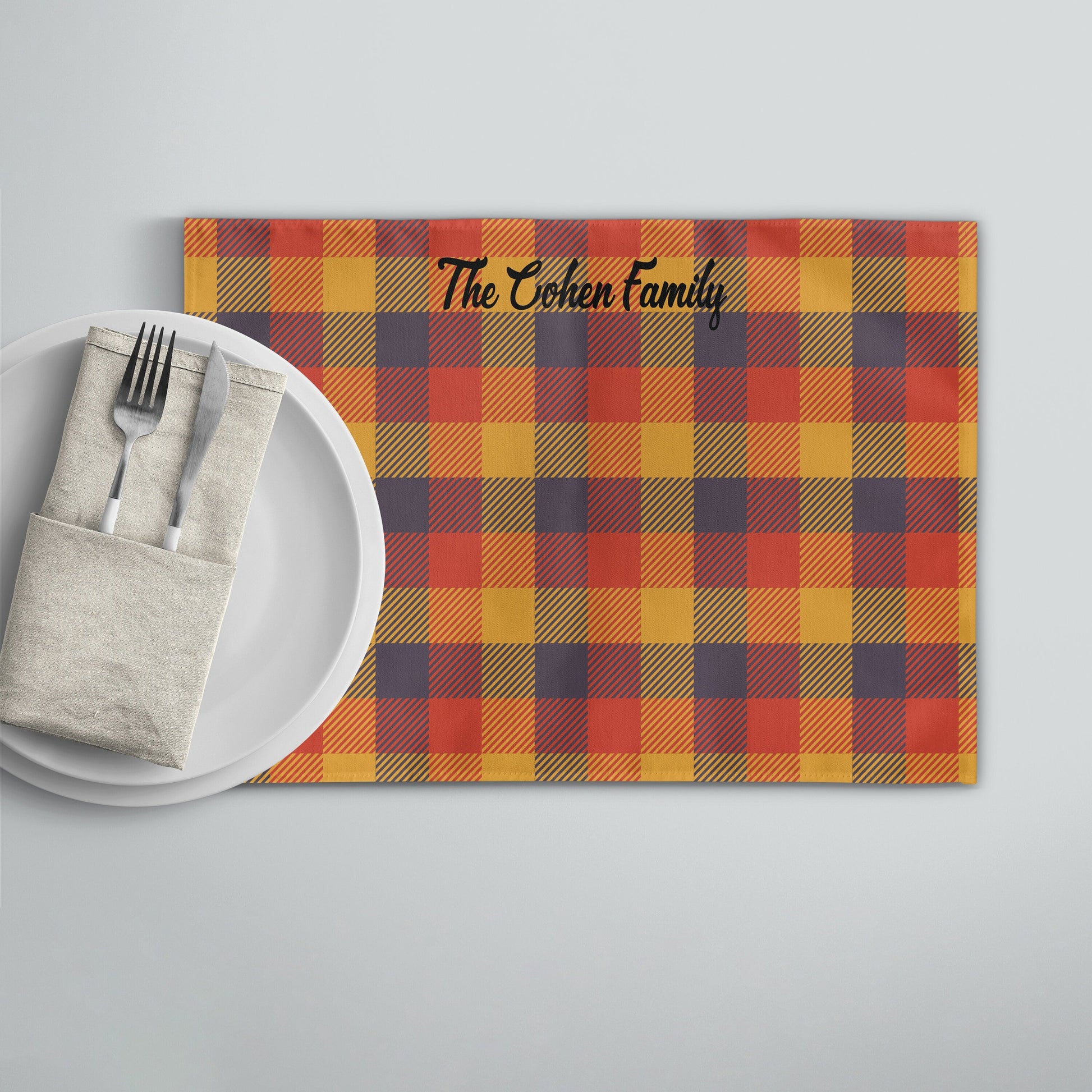 Personalized fall plaid placemat with lavender and pumpkin colors, featuring a name, on a dining table with cutlery and dish.