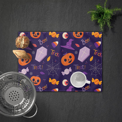 Personalized placemat with "Alex" featuring orange pumpkin, coffin, and candy on a purple background. Plate and cutlery on the left.