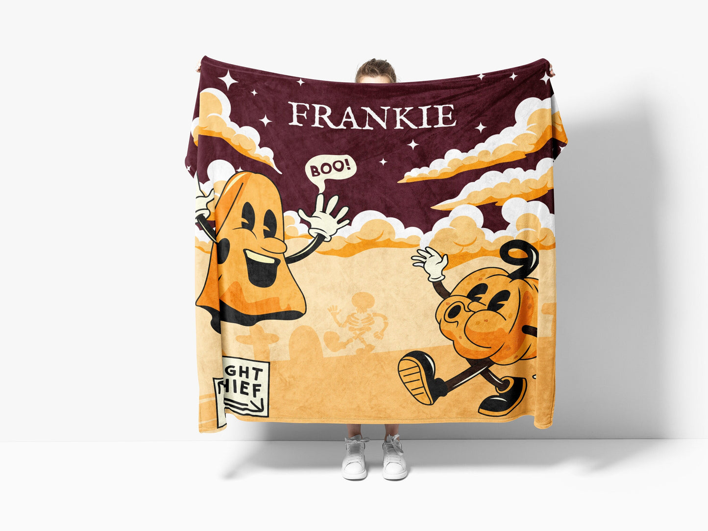 Person holding an Ouija board blanket featuring detailed whimsical ghosts, pumpkins, cloud and sky in vibrant colors.