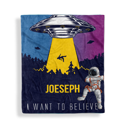 A throw blanket with alien invasion design and customized name Joseph, and a tagline 'I want to believe' displayed flat on white surface