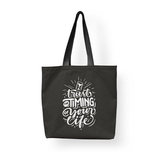 A black fashion tote bag made from cotton with the line "trust the timing of your life" printed on it